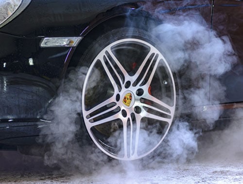 Close-up of a luxury car wheel with tire dressing applied, showing deep black finish and added shine with protective treatment.