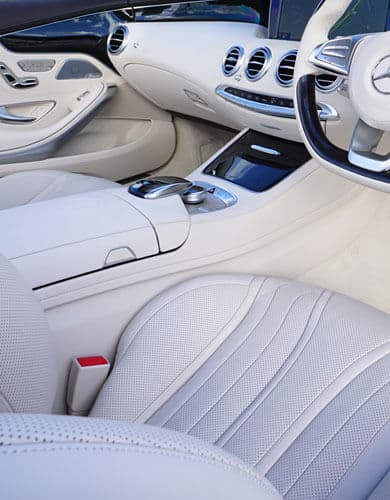 Close-up of a clean luxury car interior with leather seats and console, highlighting interior vacuuming service